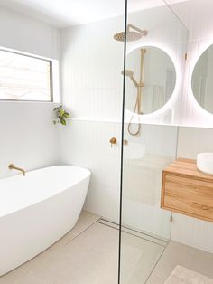 a white bath tub sitting next to a sink under two round mirrors in a bathroom