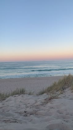 an empty beach with the ocean in the background and sand dunes to the side,