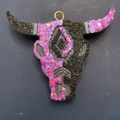 a cow's skull with pink and black glitters on it is hanging from a hook