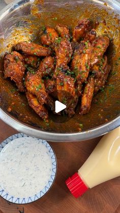 a pan filled with chicken wings and sauce on top of a wooden table next to a bottle of milk