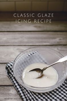 a glass bowl filled with icing on top of a checkered cloth next to a spoon