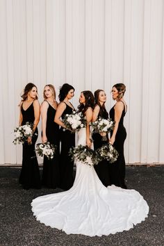 a group of women standing next to each other in front of a white wall holding bouquets