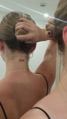 a woman with her hair in a bun is looking at herself in the mirror and has tattoos on her back