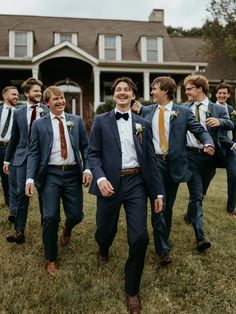 a group of men in suits and ties walking through the grass with one man wearing an orange tie