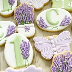 decorated cookies with lavender flowers and butterflies are displayed on a wooden surface, including one for the first birthday