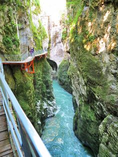 a bridge over a river in the middle of a canyon with people walking on it