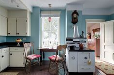 a kitchen with blue walls and white cabinets has two chairs in front of the stove