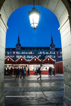 people are walking through an archway in the middle of a street at night with lights on