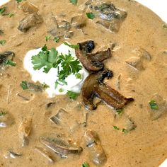 a bowl of soup with mushrooms and sour cream on top, garnished with parsley