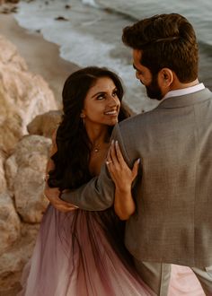 a man and woman standing next to each other near the ocean with their arms around each other