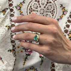 a woman's hand wearing a gold ring with an emerald colored stone on it