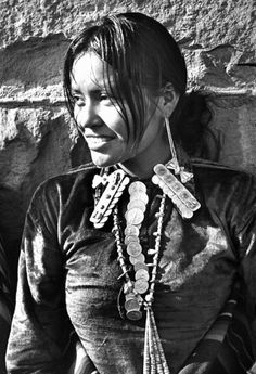 black and white photograph of a woman with necklaces on her neck, standing in front of a stone wall