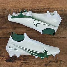 a pair of white and green soccer cleats sitting on top of a wooden floor