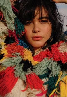 a woman wearing a colorful scarf with fringes on her head and hands behind her head