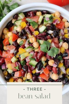 a white bowl filled with beans and veggies next to tomatoes, cilantro