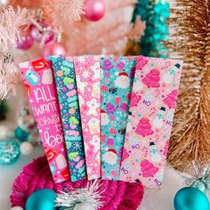 colorful christmas wrappings are sitting on a table next to ornaments and trees with pink, blue and green decorations