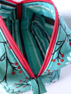 the inside of a purse with red zippers and flowers on blue fabric, sitting on a white surface