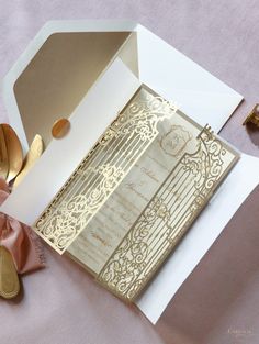 the inside of a wedding card with gold foil on it next to some shoes and a pink ribbon