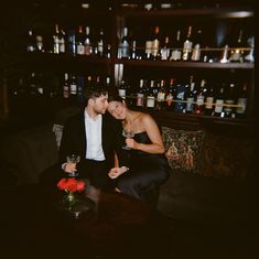 a man and woman sitting at a table with wine glasses in front of the bar