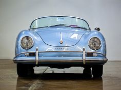 an old blue sports car is parked in a room with wood flooring and white walls