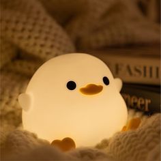 a small light that looks like a ducky sitting on top of a bed next to a book