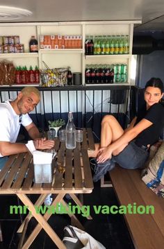 a man and woman sitting at a table in front of shelves with bottles on it