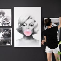 a woman standing in front of pictures on the wall with her tongue sticking out and blowing bubbles