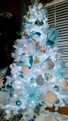 a white christmas tree decorated with blue and silver ornaments, seashells and starfish