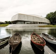 three canoes are tied to the dock in front of a building with a curved roof