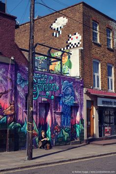 a mural on the side of a building in front of a woman sitting on a bench