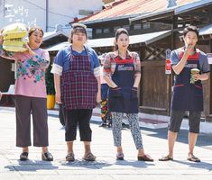 four young women standing in front of a building with food on their heads and one wearing an apron