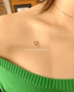 the back of a woman's shoulder with a small heart tattoo on her chest