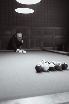 two men playing pool in a dark room with several balls on the table and one man leaning over