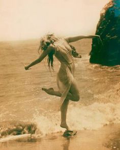 a woman standing on top of a wave covered beach next to the ocean with her arms outstretched