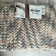 a close up of a knitted blanket on a bed with a magazine laying next to it