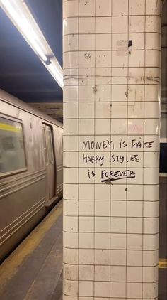 a subway station with graffiti written on the wall next to a silver and white train