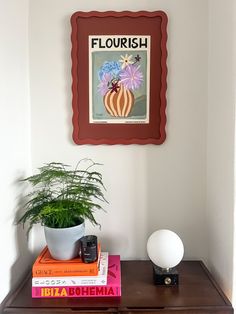 a wooden table topped with books and a potted plant next to a wall hanging