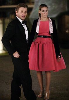 a man and woman in formal wear standing next to each other on the street at night