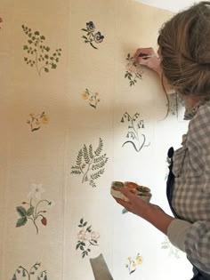 a woman is painting the wall with flowers on it and she is holding a paintbrush