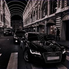 two black cars parked on the street in front of an old building at night time