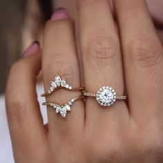 a woman's hand holding two rings with diamonds on them and one is wearing an engagement ring