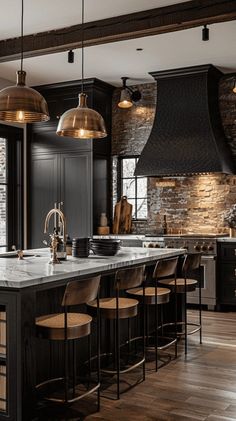 a large kitchen with black cabinets and gold pendant lights hanging from the ceiling, along with bar stools