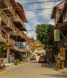 people are sitting on the sidewalk in front of some shops and buildings with thatched roofs