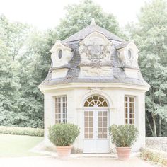 a white building with two potted plants in front of it and trees behind it