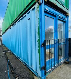 a blue and green shipping container sitting on top of a street next to a fence