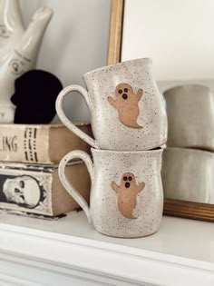 two coffee mugs with ghost faces on them are sitting on a mantle in front of a mirror