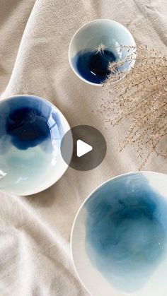 three bowls with blue and white designs on them sitting on a table cloth next to a plant