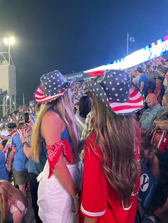 two women in patriotic hats standing next to each other at a sporting event with fans