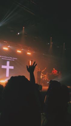 a person raising their hand up in front of a cross on a stage with lights