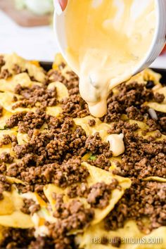 someone is adding cheese to nachos in a pan with meat and sauce on top